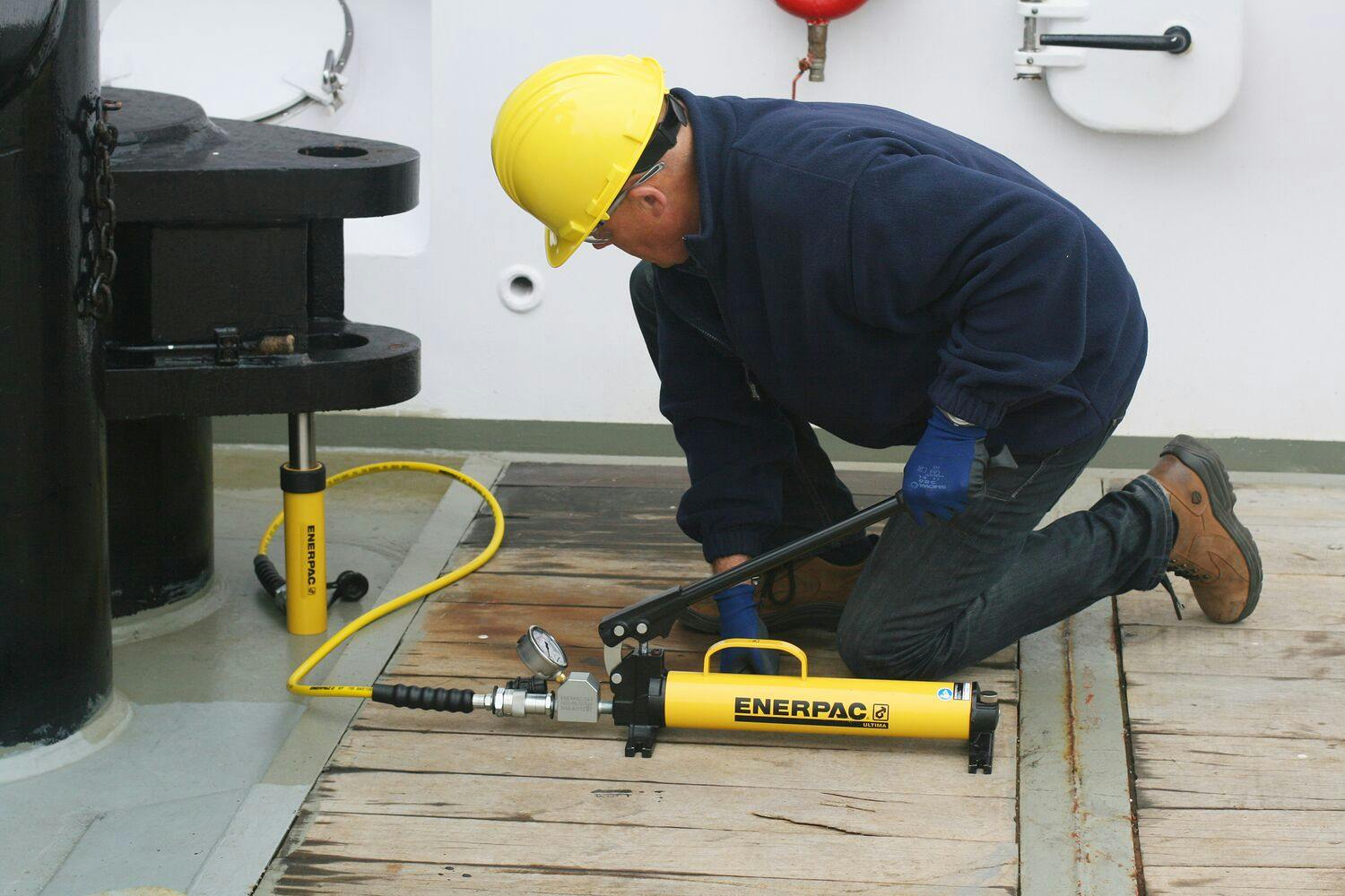Arbeider som bruker hydraulisk pumpe med manometer og sylinder. Løfter utstyr ombord på en båt.
